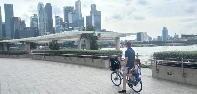 Un père et sa fille en balade à vélo contemplent la skyline moderne de Singapour au bord de Marina Bay.