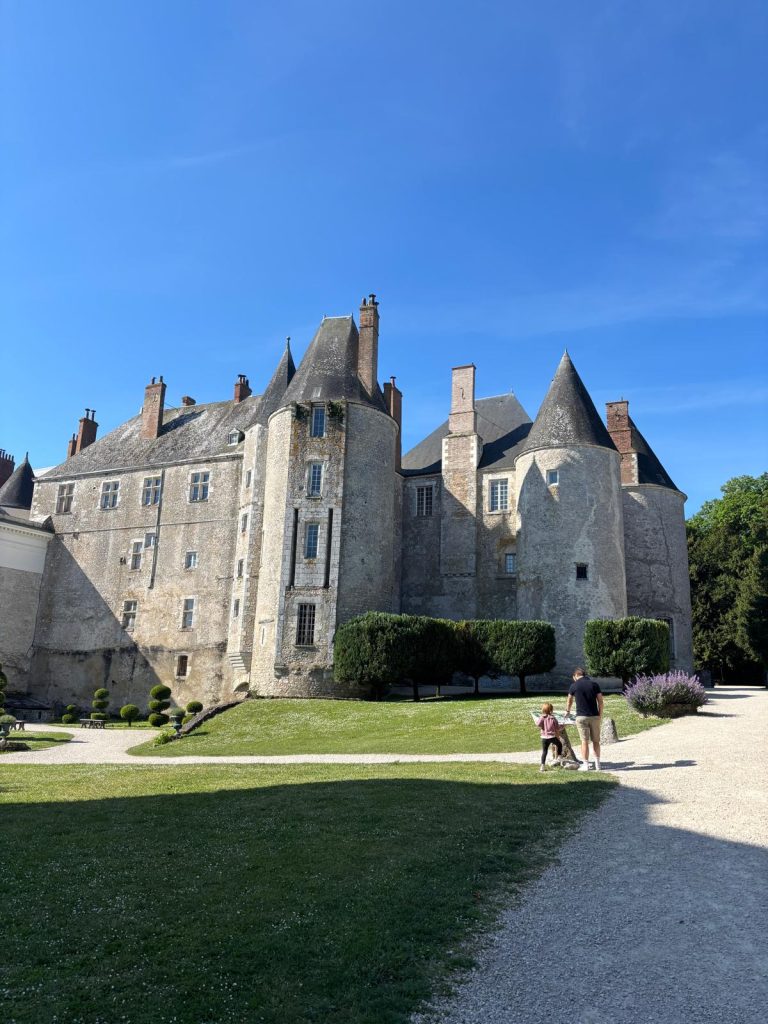 week-end-en-famille-meung-sur-loire.jpg Vue d’ensemble du château de Meung-sur-Loire prise depuis l’entrée principale, avec une famille marchant sur l’allée gravillonnée un jour ensoleillé.